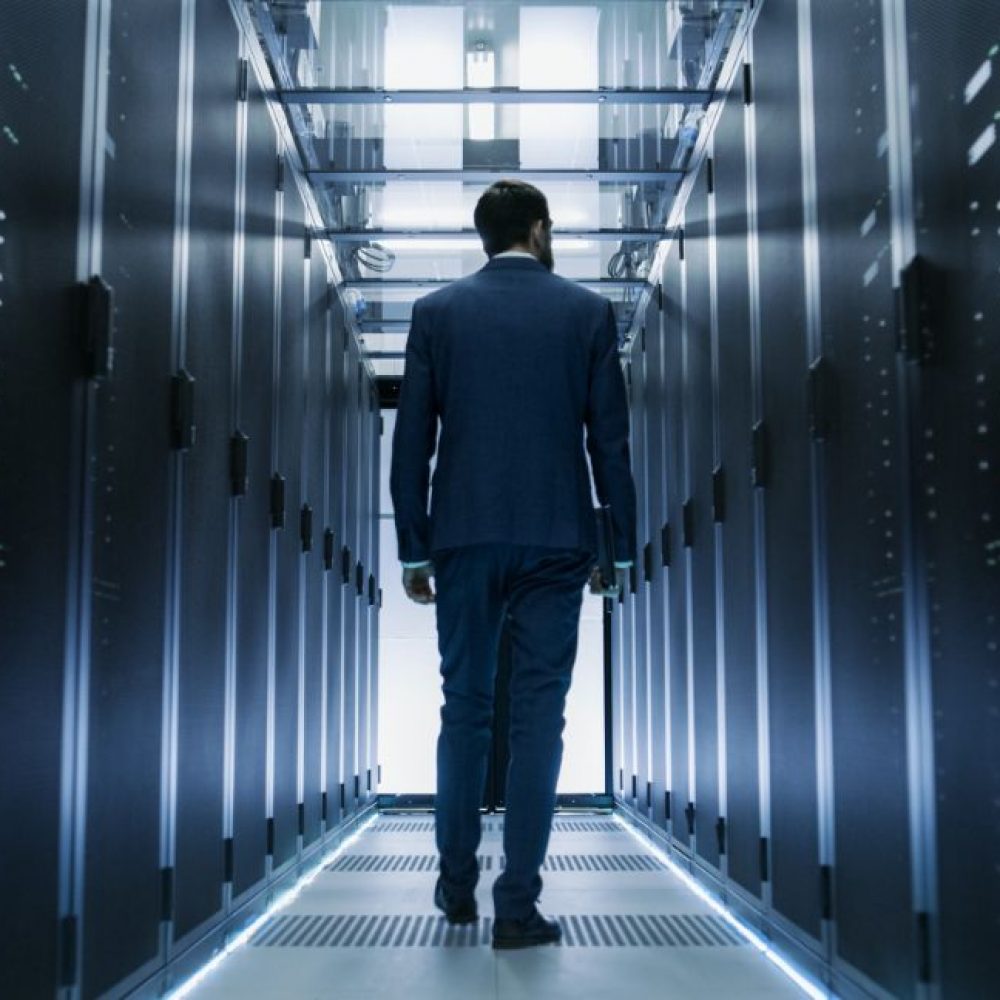 Canva - Following Shot of IT Engineer Walking Through Data Center with Rows of Working Rack Servers on Both Sides. (1)